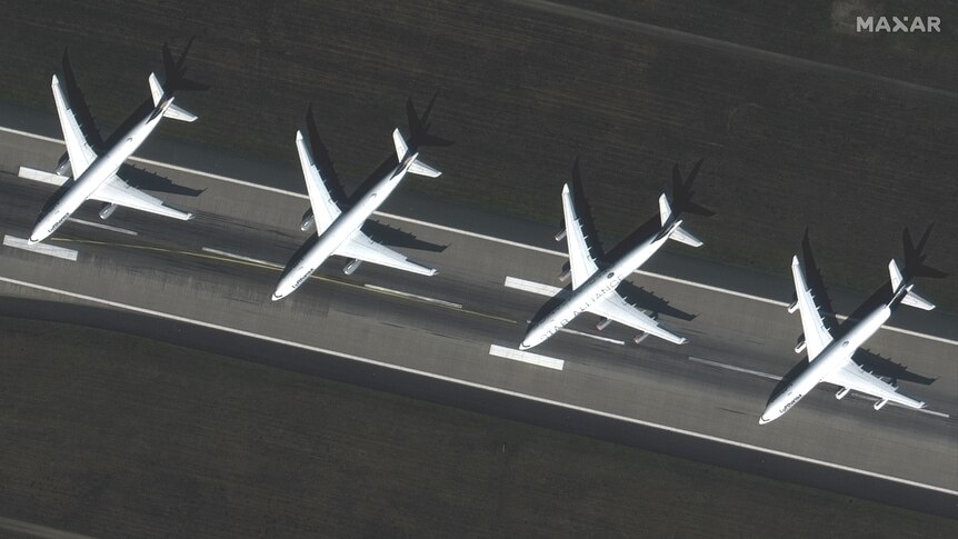 A satellite image shows four passenger planes parked and idle on a runway