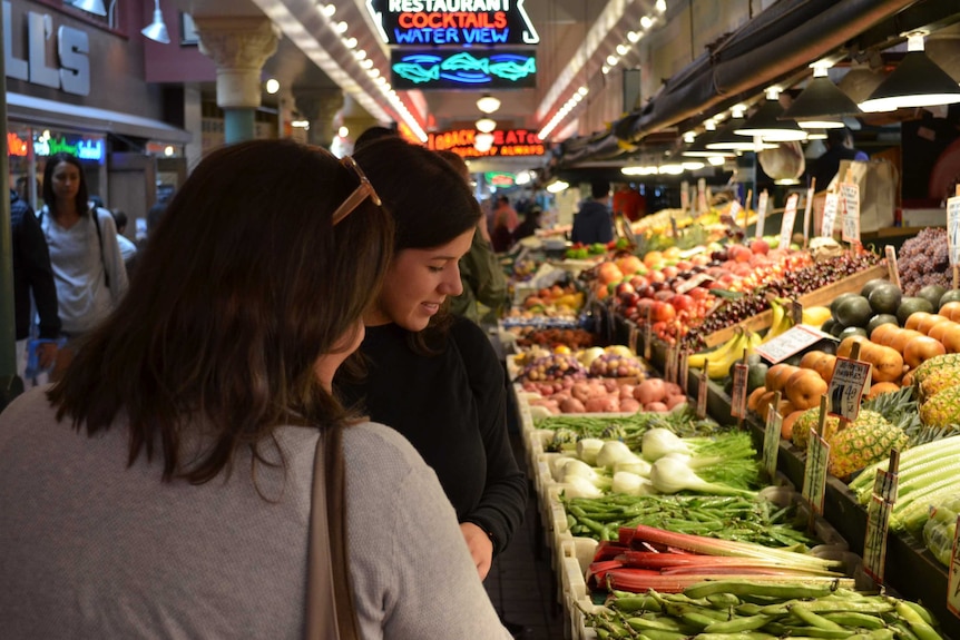 Two women shop for veggies in a market