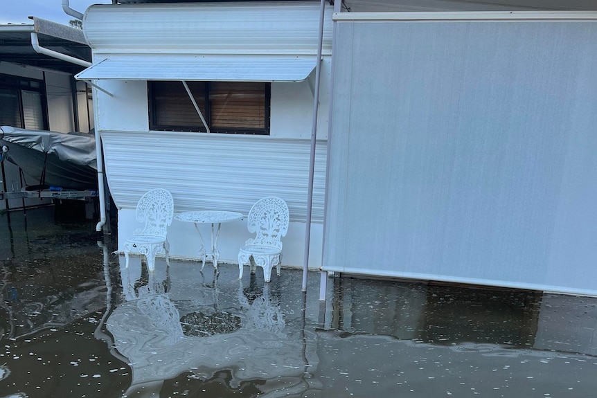 White caravan with two white chairs partially submerged in water