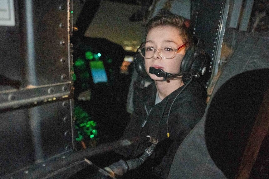 A young kid with glasses inside a helicopter. 