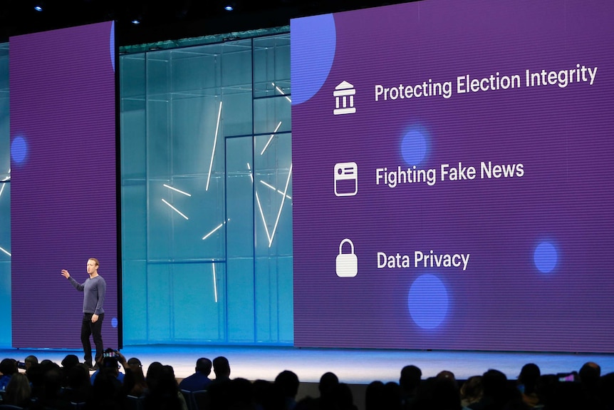 Mark Zuckerberg stands in front of huge screens as he speaks at a conference.