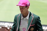 Wearing a green blazer, whites and a pink baggy cap, Tim Paine walks through up the SCG race past members seats