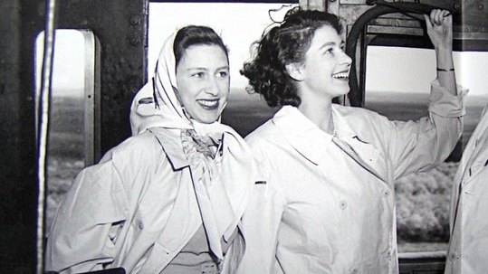 Queen Elizabeth and Princess Margaret as young women, dressed in trenchcoats