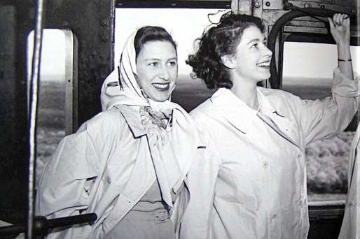 Queen Elizabeth and Princess Margaret as young women, dressed in trenchcoats