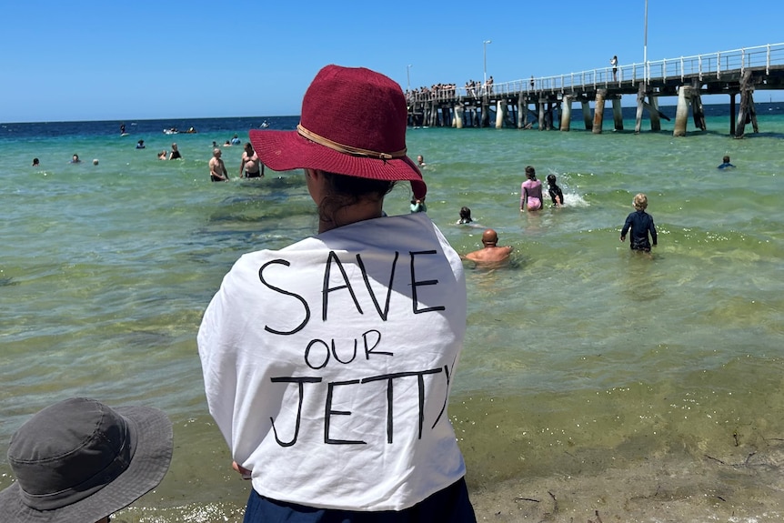 woman at shore with writing on back of t-shirt saying save our jetty