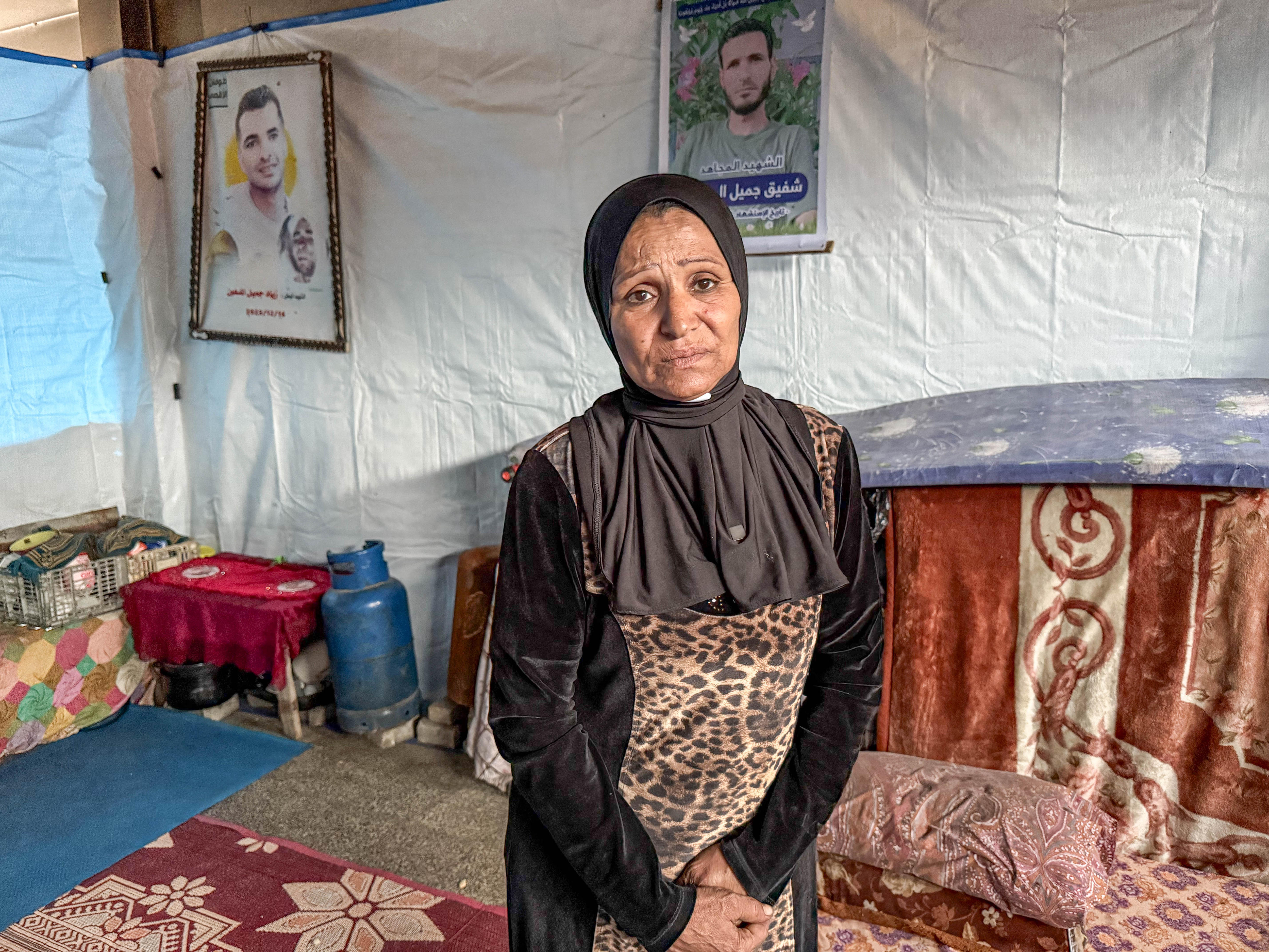 A woman stands in front of pictures of two of her sons hanging on a wall in her home.