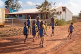 A group of primary school-aged kids in school uniforms walking on a red dirt road. 