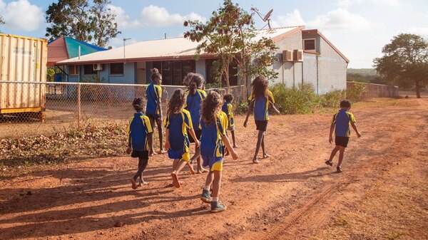 A group of primary aged kids in school uniforms walking on a red dirt road.