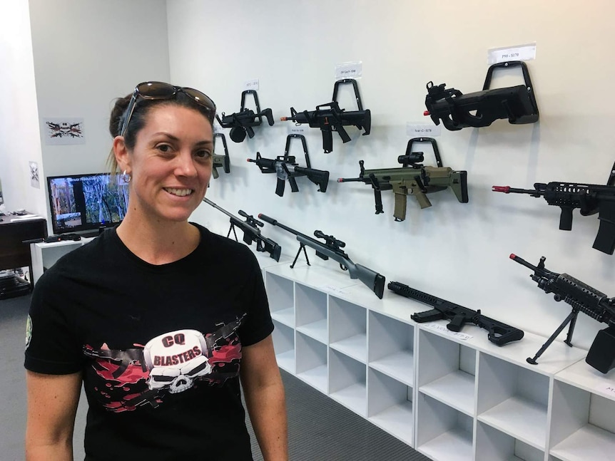 A woman stands in front of a wall of gel blasters (replica guns)