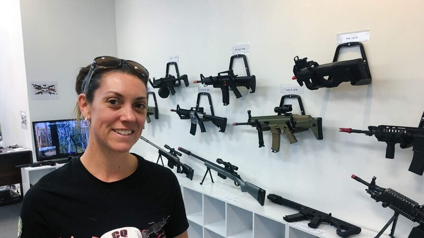 A woman stands in front of a wall of gel blasters (replica guns)