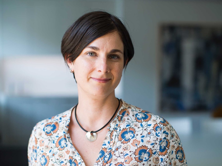 Laurie Berg poses for a portrait photograph. Her hair is dark and short, sweeping over her forehead. She wears a floral shirt.