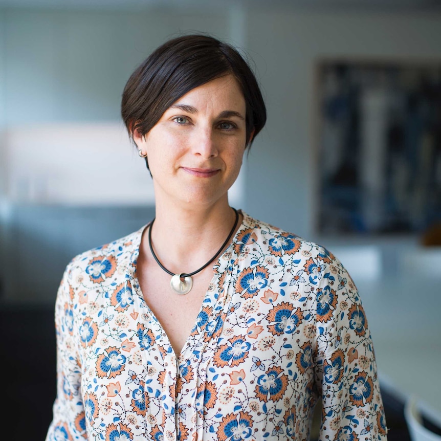 Laurie Berg poses for a portrait photograph. Her hair is dark and short, sweeping over her forehead. She wears a floral shirt.