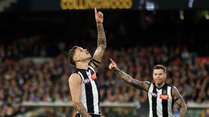A Collingwood AFL player stands and points to the sky after kicking a goal.
