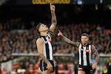 A Collingwood AFL player stands and points to the sky after kicking a goal.