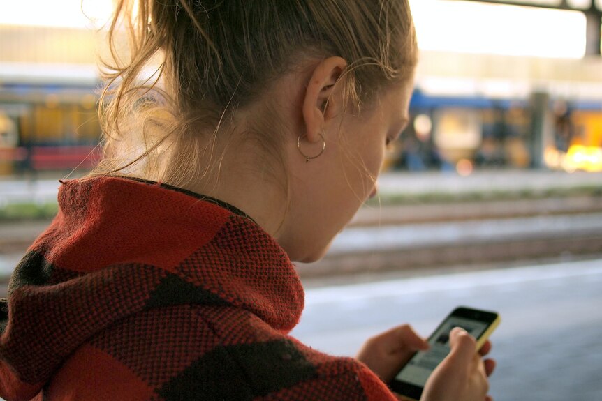 A young woman in a red hoodie uses a smartphone