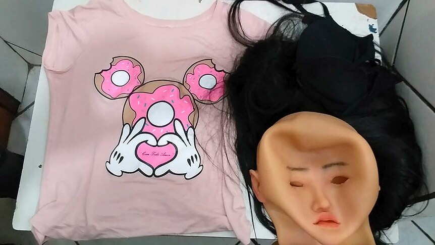 A pink shirt, bald cap mask and a wig laid out on a table.