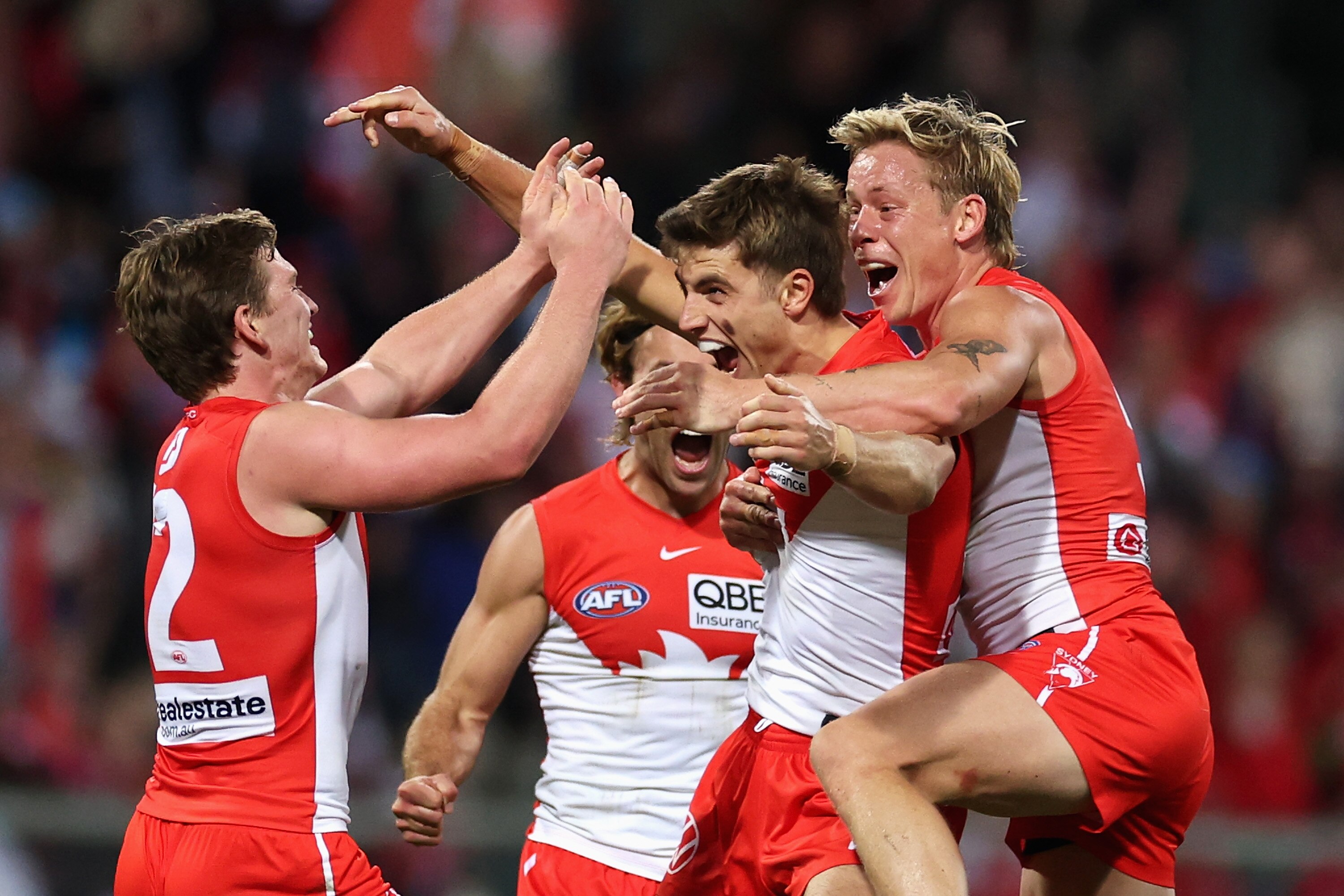 A group of AFL players in red and white huddle, celebrating a victory