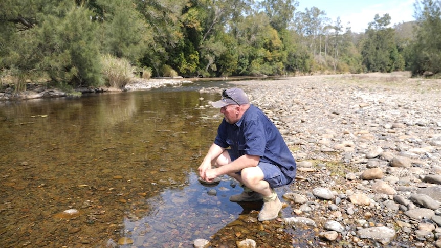 Craig squatting by a dwindled stream on a dry river bed pondering how he will get through this drought.