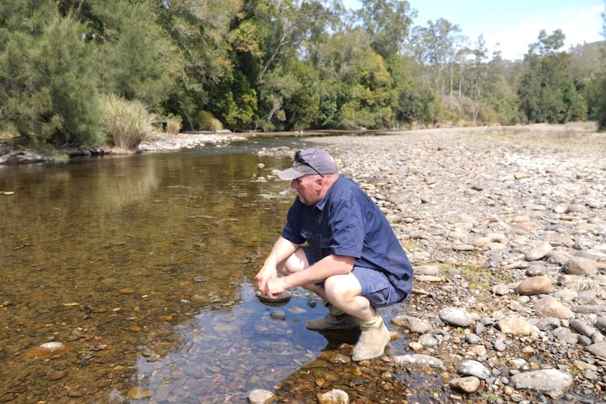 Craig squatting by a dwindled stream on a dry river bed pondering how he will get through this drought.