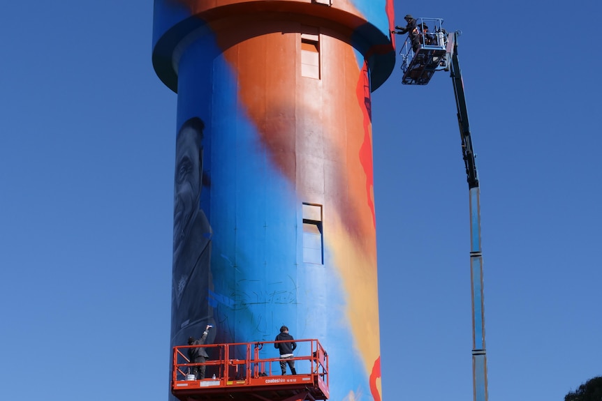 Colourful water tower with men painting in cherry pickers