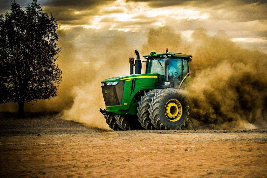 A tractor with a large plume of dust behind it captured in motion.