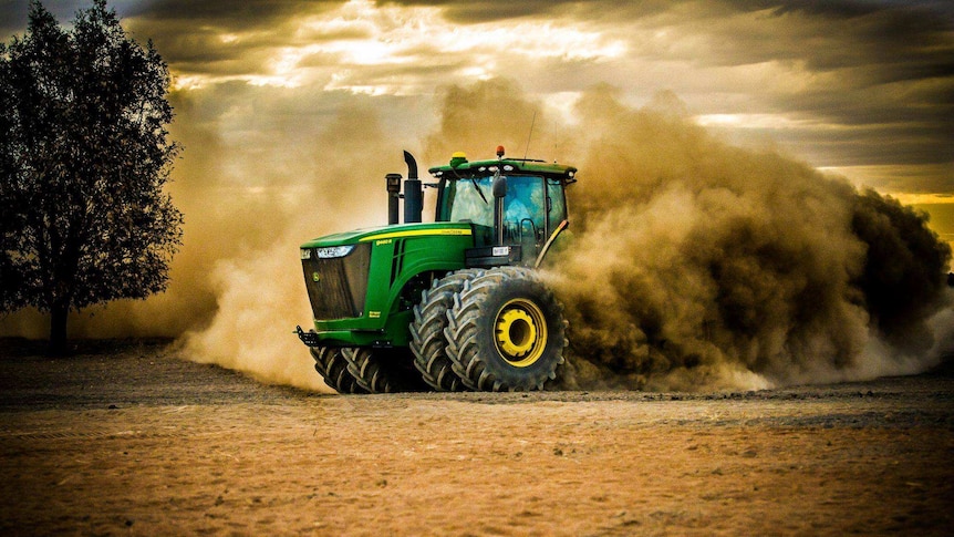 A tractor with a large plume of dust behind it captured in motion.
