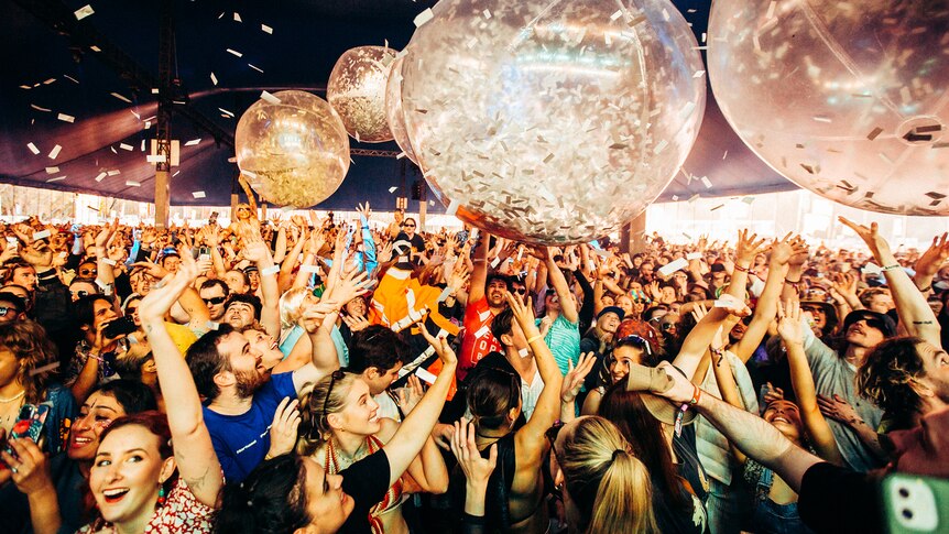 Festival crowd bouncing large plastic balls filled with silver confetti.
