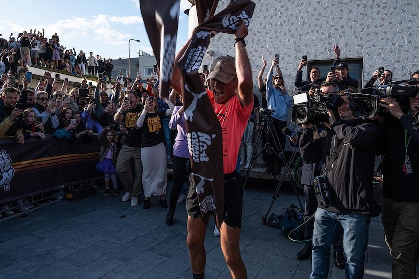 A man holds the finish sash in the air with a crowd around him