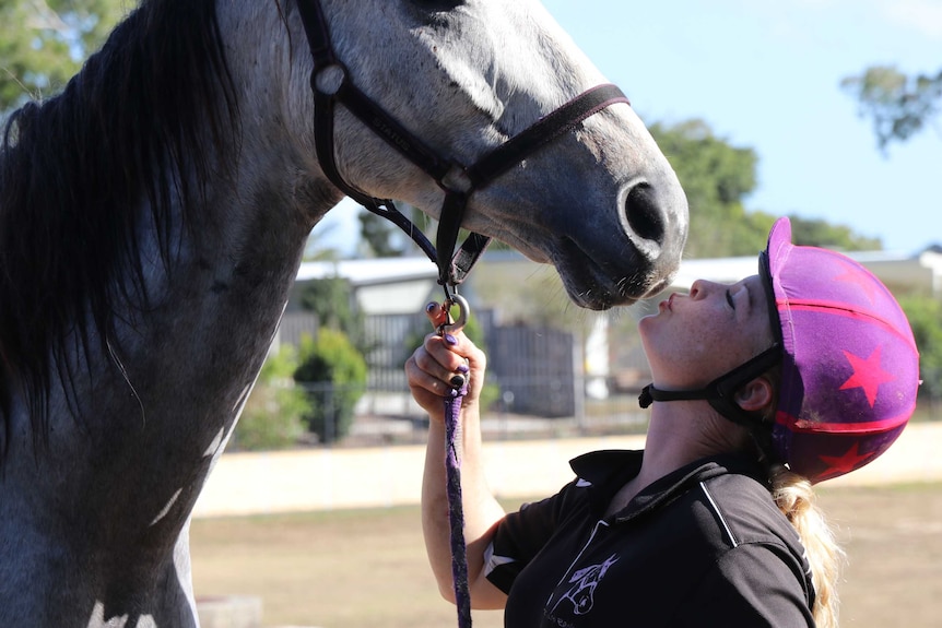 A woman in a riding helmet kissing a horse