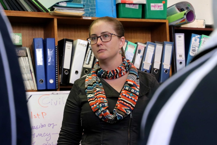 Elar stands in front of file binders, looking at two students.