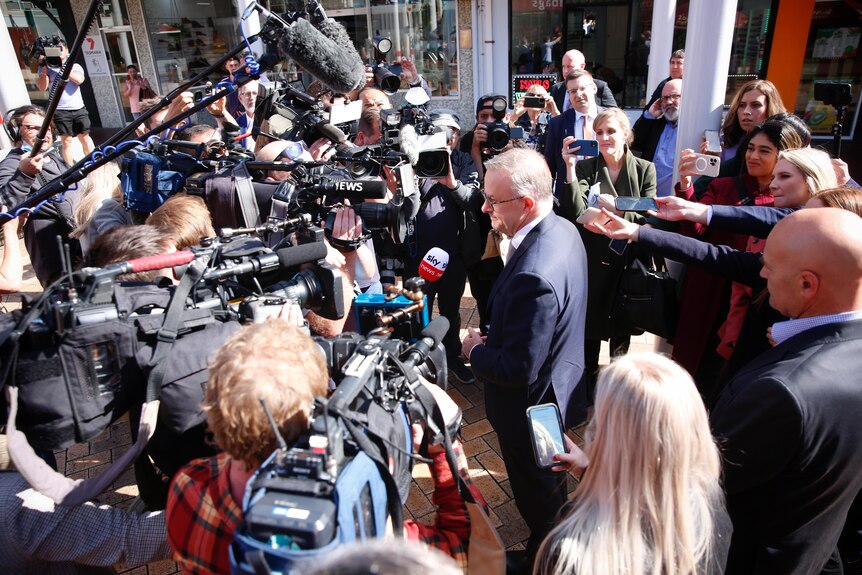 A man surrounded by a ring of journalists holding cameras and microphones