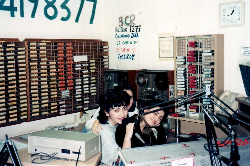 Three young women sit close together in a radio studio