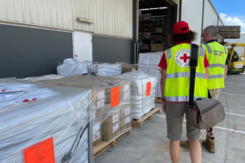 Two Red Cross workers at a warehouse full of aid supplies.