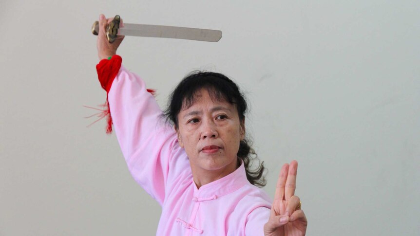 A woman in traditional chinese outfit holding a sword doing a tai chi pose