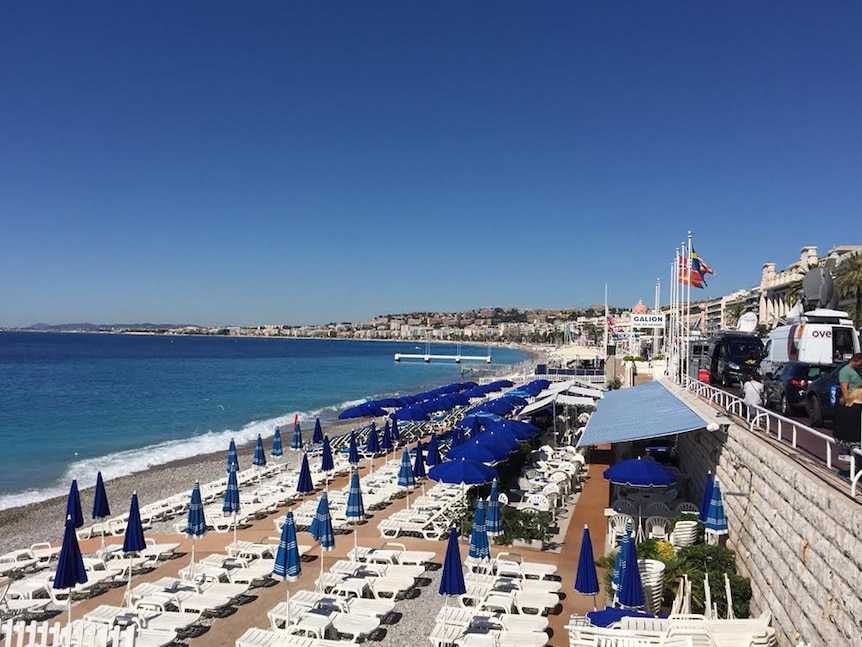 An empty beachfront in Nice, with news vans parked on the road above