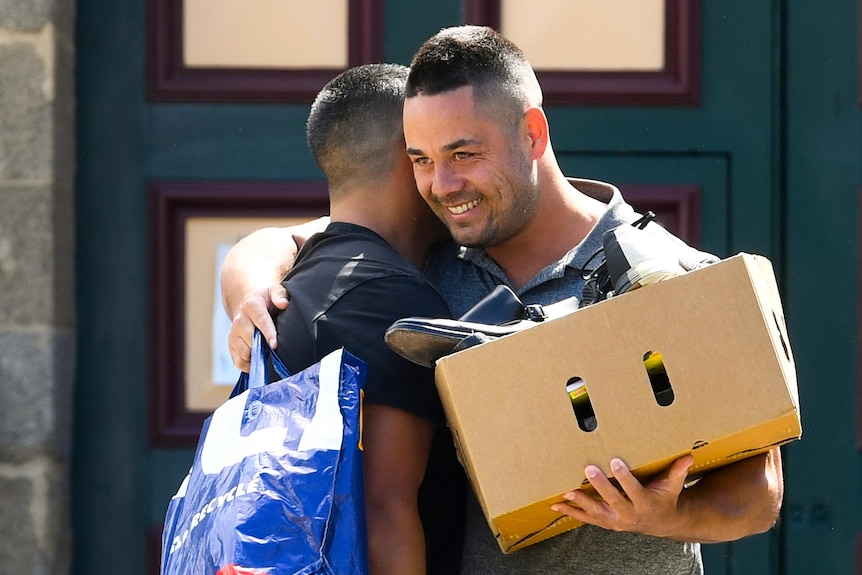 A man holding a cardboard box hugs another man