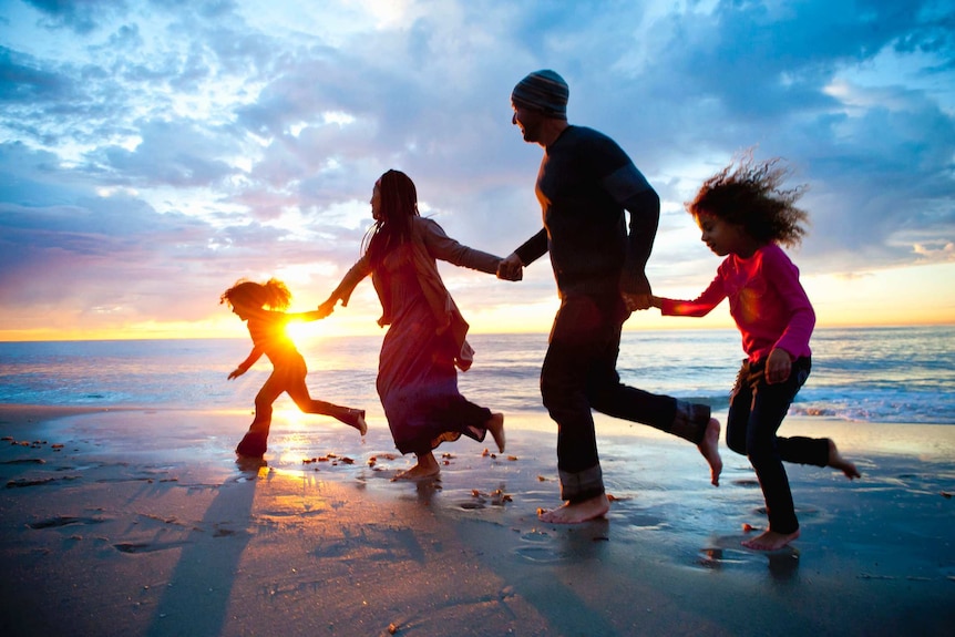 Four people, silhouetted by the sun behind them, run along a beach