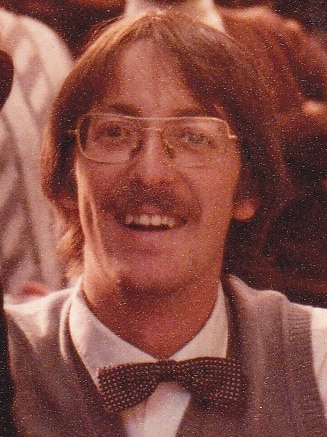Grainy headshot of Sunderland with long hair, moustache, glasses and wearing a bow tie and vest.