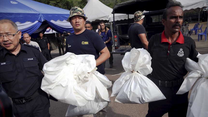 Forensic policemen carry body bags at the site of human trafficking camps