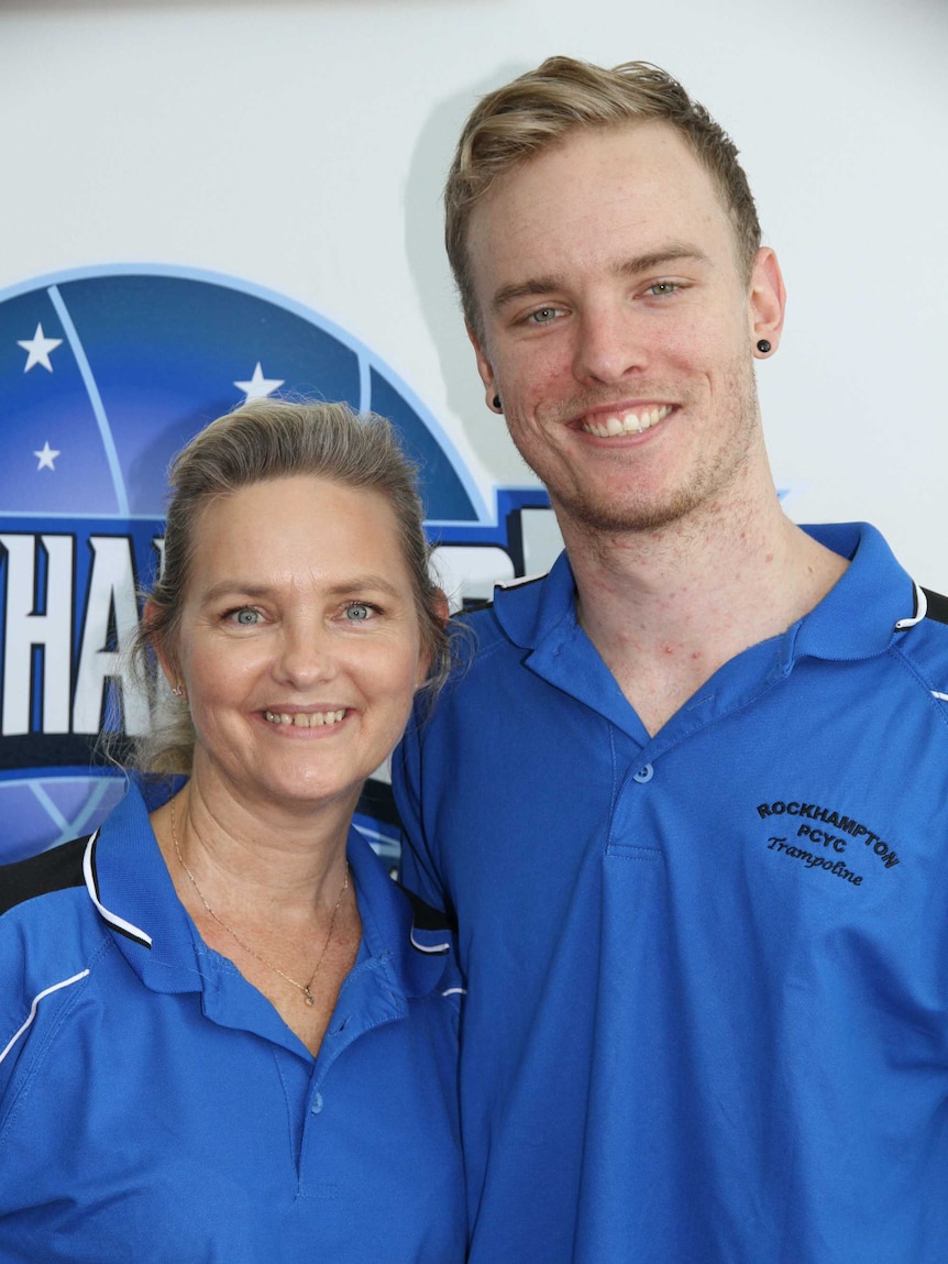 A short blonde woman standing with a taller younger man both wearing blue t shirts