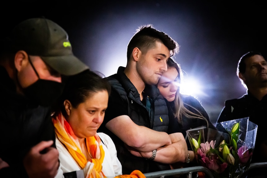 People looking sad at night near Shane Warne's statue.