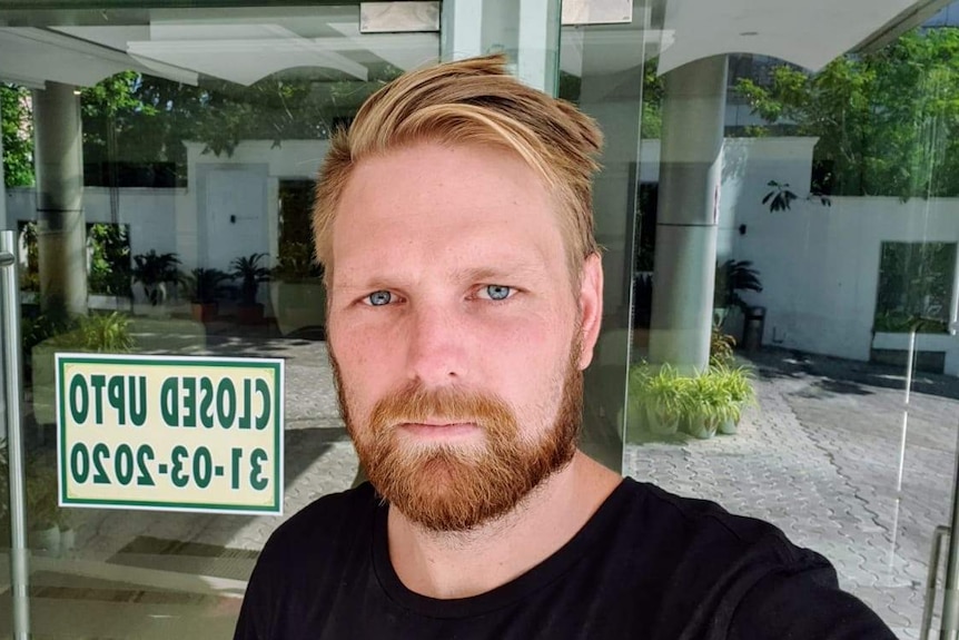 A blonde bearded man looking serious in an empty hotel lobby