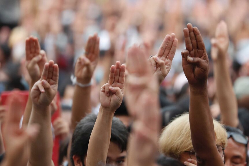 People raise their hands in the air with three fingers pointed in the sky.