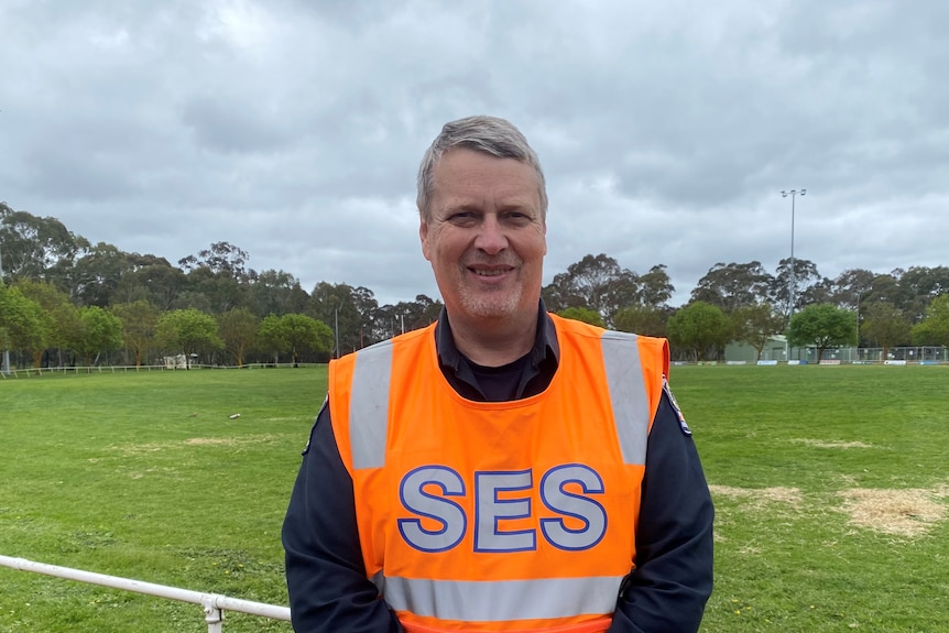 A man wearing an orange vest with SES written on it stands on an oval
