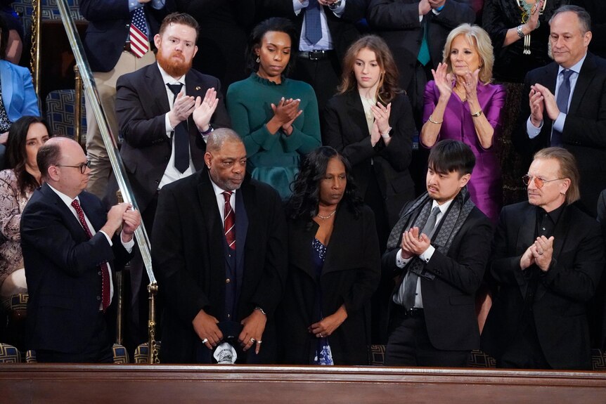 A crowd including Jill Biden and Bono stands to applaud a couple in the centre with sincere expressions on their faces