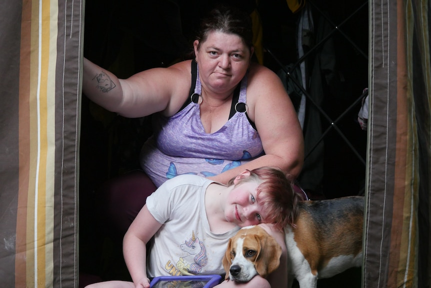 A woman and her daughter and their dog outside a caravan.