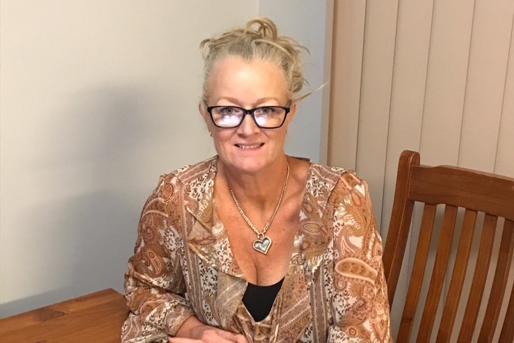 A woman sits at a dining table with a laptop