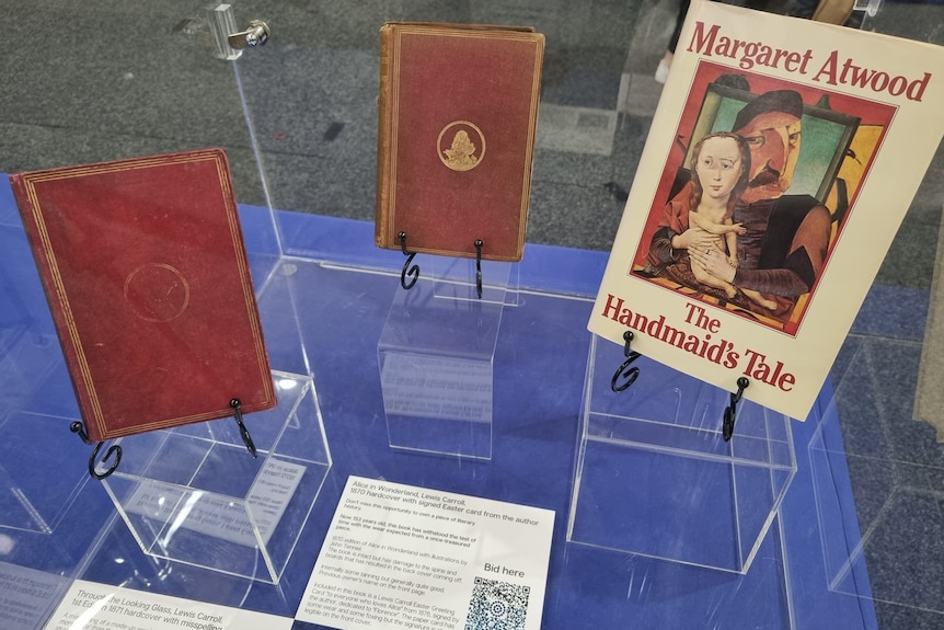 Three vintage books sit in a display cabinet, with red and gold covers.