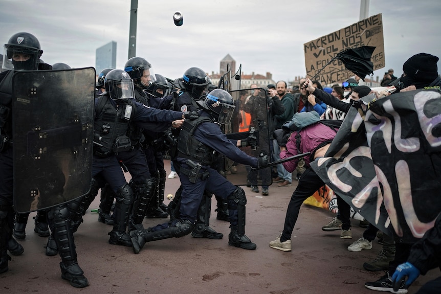 Police in riot gear hit protesters with a baton during clashes in the French city of Lyon