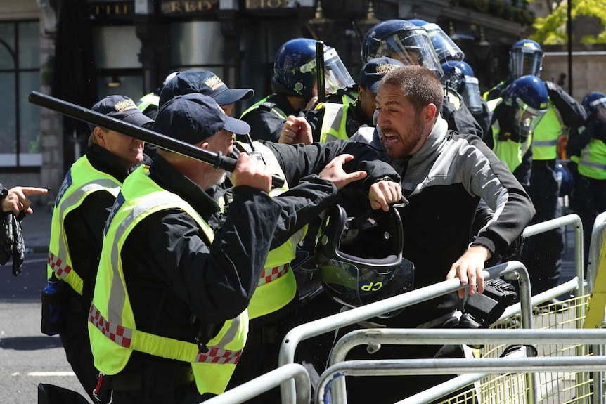 Police use batons to control a protesters screaming and lashing out at them over a barrier.